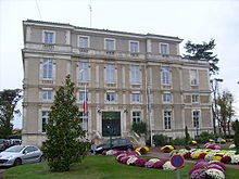 Photographie d'un bâtiment de quatre étages, crépis et bordures de pierre, de style classique à pilastres et colonnades