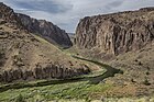 View over a river bend in a shrubby desert landscape framed by vertical cliffs