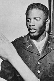 Black man in military uniform featuring the crossed-sabre insignia of a U.S. Cavalry unit receives a salute from a person out of view