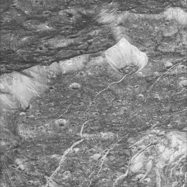 Differently sized and oriented fractures within 60-km crater Amastrus (central peak at lower right). Larger arcuate fractures running from lower left to upper right are the Padua Chasmata, whereas smaller more parallel fractures from lower right to upper left may be related to the Aurunca Chasmata.