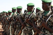 Soldiers lined up in a row, with green caps, carrying rifles