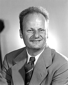 Photo en noir et blanc. Visage d'un homme avec un grand front et souriant portant un veston.