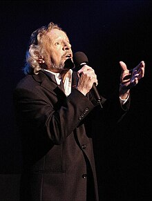 Photo du chanteur debout, le micro à la main, en train de chanter.