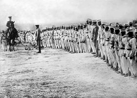 Photographie montrant des soldats mexicains debout et alignés, vêtus d'uniformes beige, passés en revue par un gradé monté à cheval.