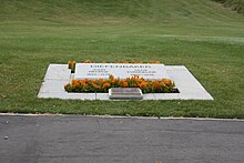 Plaque de marbre portant les noms de John et Olive Diefenbaker se trouvant au milieu d'une pelouse et entourée de fleurs jaunes et d'une petite plaque de bronze.