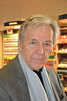 Photograph of the head and shoulders of a man who is looking somewhat to the left of the camera. He has a slightly quizzical smile. He is wearing a dark green sports coat and a pullover shirt.