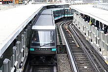 Vue plongeante sur la station Bastille de la ligne 1. Au premier plan, sur la voie de gauche les deux premières voitures de la rame MP 89 CA sont rectilignes ; au deuxième plan, les caisses de la même rame dans le creux du virage.