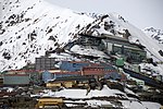 A mining town located on a steep slope. Buildings have facades in different colours and the mountains are covered by snow.