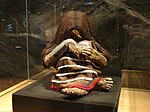 A replica of the Plomo mummy, a child in a sitting position with crossed hands and braided hair