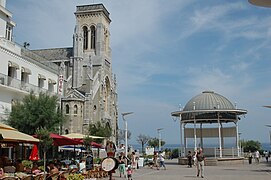 Vue de la tour-porche d'une église ; esplanade au premier plan ; la mer en arrière plan.