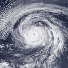 A satellite image of a well-organized hurricane with a tightly wound circulation, spiral bands fanning out, and a clear eye; an arc of thin, high clouds is to the north and northwest of the hurricane