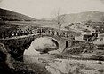 Soldaten ziehen einen Feldbahnwagen mit Muskelkraft über eine historische Bogenbrücke