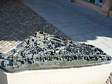 Blick von schräg oben auf ein in der Wittenberger Innenstadt aufgestelltes Reliefmodell, das auf einem etwa hüfthohen Sockel aus weißem Stein ruht. Das Relief ist aus Bronze und hat einen etwa dreieckigen Grundriss. Es zeigt in modellhafter Darstellung Gebäude, Straßenzüge, Plätze und Baumgruppen; die Häuser sind wenige Zentimeter hoch. Am vorderen Rand sind zwei Texttafeln in erhabener Normalschrift und in Brailleschrift angebracht, auch einige ausgewählte Plätze und Gebäude sind in dieser Weise beschriftet.