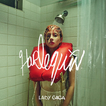 Gaga with red-dyed hair standing below an operating shower head wearing a white clothed-dress with a personal flotation device around her neck