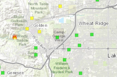 Map zoomed in on Golden,  Colorado with a fire symbol denoting the location of the Goltra Fire. Yellow squares to the right of the fire show light smoke impacts. South of the fire, green boxes denote good air quality.