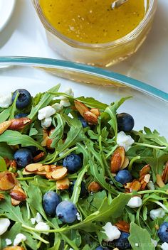 a salad with blueberries and almonds in a glass bowl on a white table