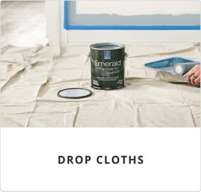 Drop cloths. A person rolling paint in a paint tray next to a can of Emerald on top of a drop cloth.