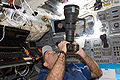 John Grunsfeld uses a still camera at an overhead window on the aft flight deck of Space Shuttle Atlantis during flight day three activities.