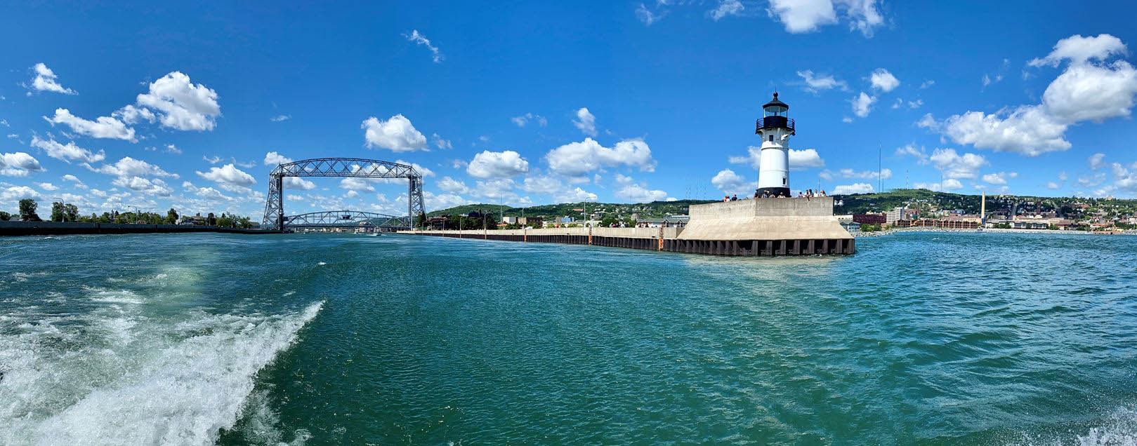 Aerial Lift Bridge and a lighthouse at the end of a pier from the back of a motorboat.