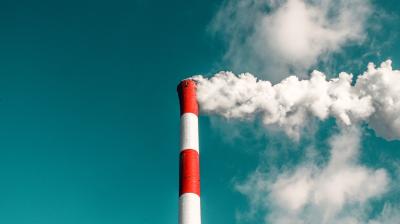 Industrial smokestack emitting white smoke against a blue sky.