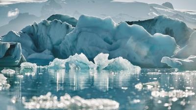 Glacial icebergs floating in a calm, icy water with a hazy mountain backdrop.