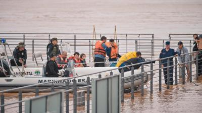 Rescue workers and divers preparing on a dock with boats on a muddy river, likely in response to an emergency.