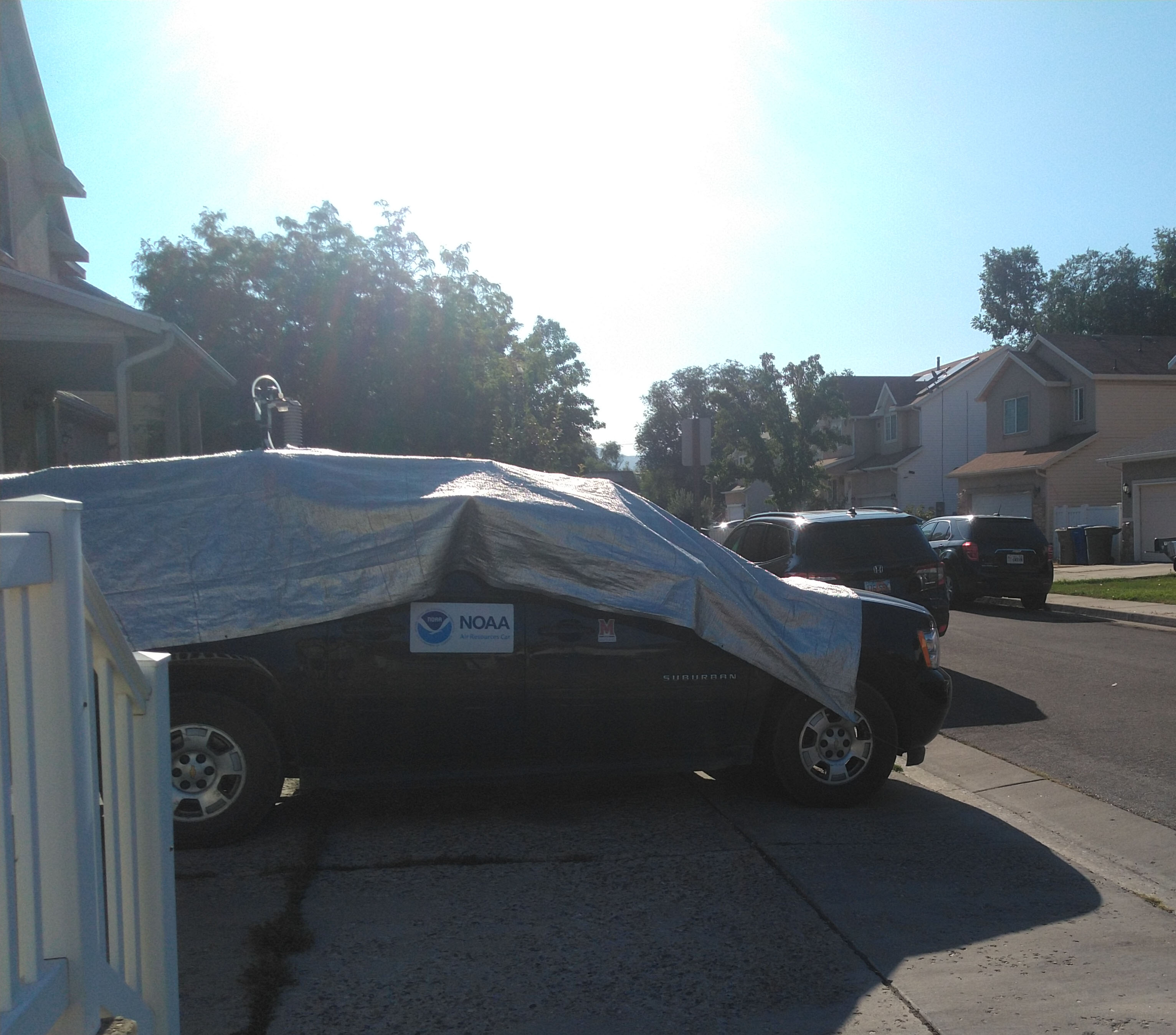 SUV in a driveway with a silver tarp draped over it.