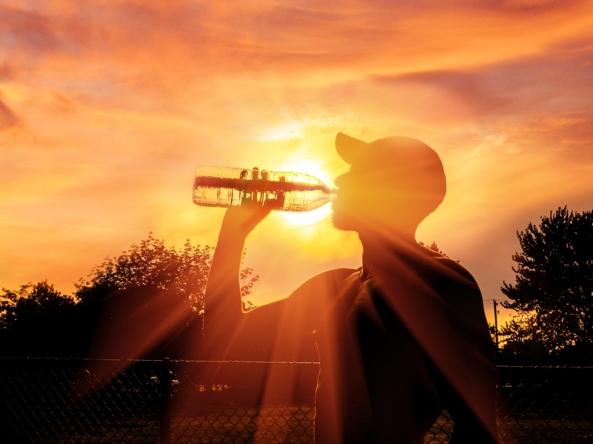 Silhouette of a man drinking water in a wooded area. Strong sunlight beams from the background. 