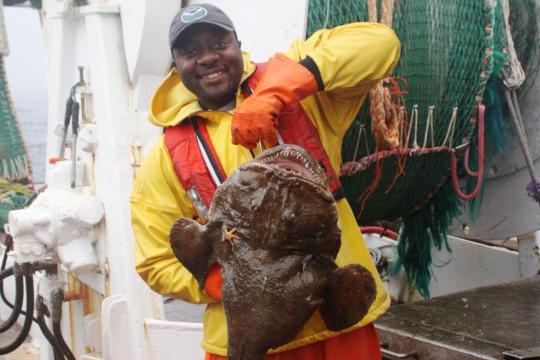 Calvin Alexander in yellow and orange gear holding large monkfish.