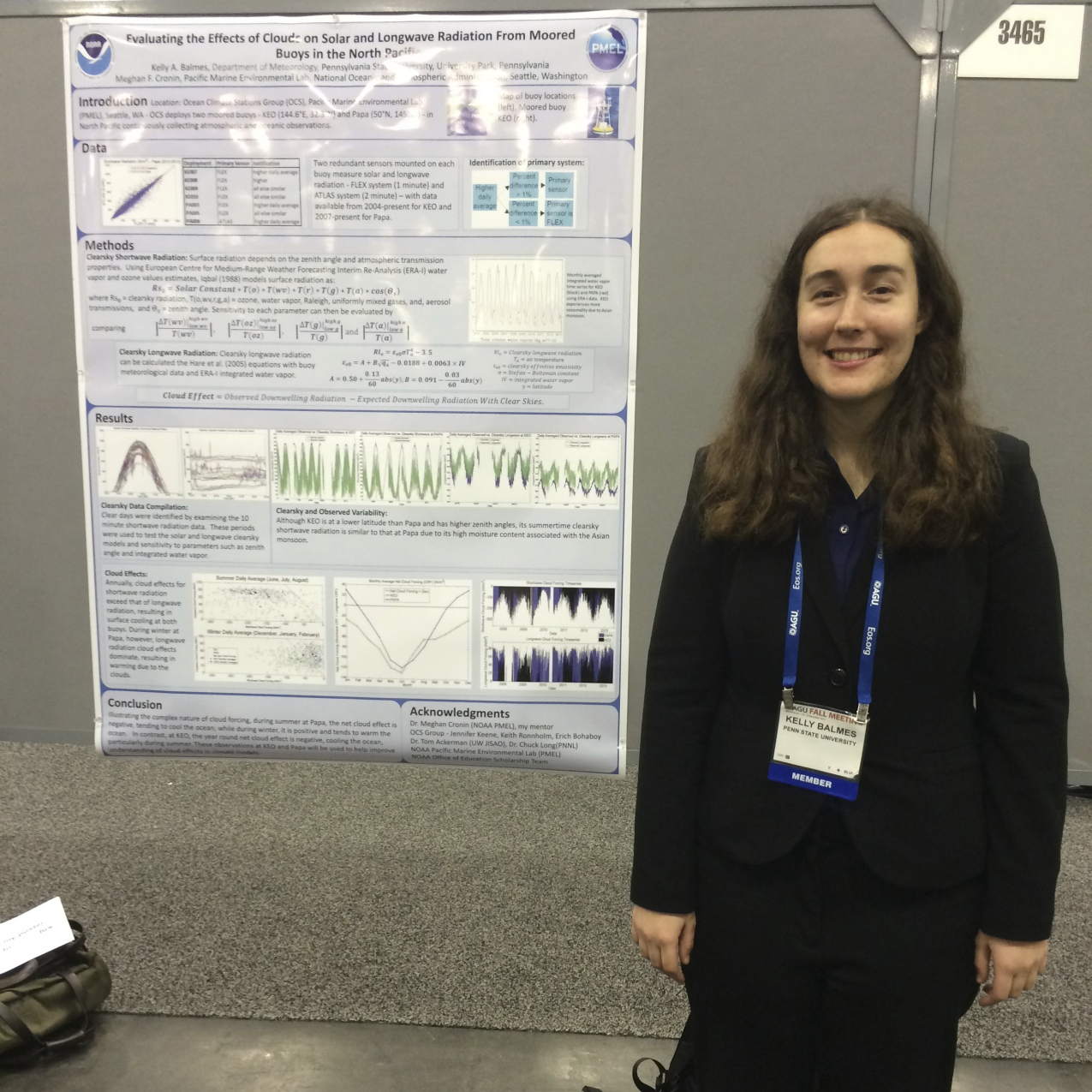 Kelly poses, smiling, next to her conference poster She's wearing a suit and name tag.